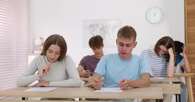 Students taking exam at wooden table indoors
