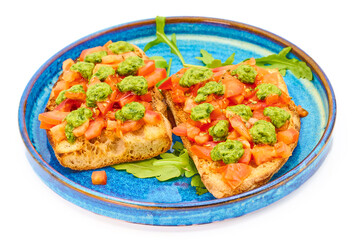 Italian bruschetta with fresh tomatoes, pesto and crusty bread on a blue plate with a white background