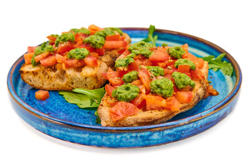 Italian bruschetta with fresh tomatoes, pesto and crusty bread on a blue plate with a white background