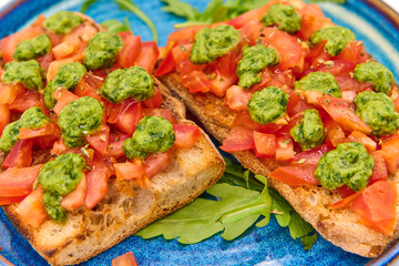 Italian bruschetta with fresh tomatoes, pesto and crusty bread on a blue plate with a white background