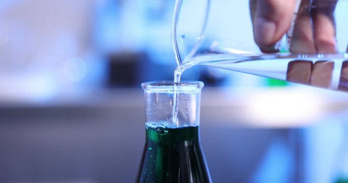 Woman pouring liquid from glass beaker into flask in laboratory, closeup