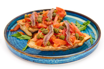 Italian bruschetta with fresh tomatoes, capers, anchovies and crusty bread on a blue plate