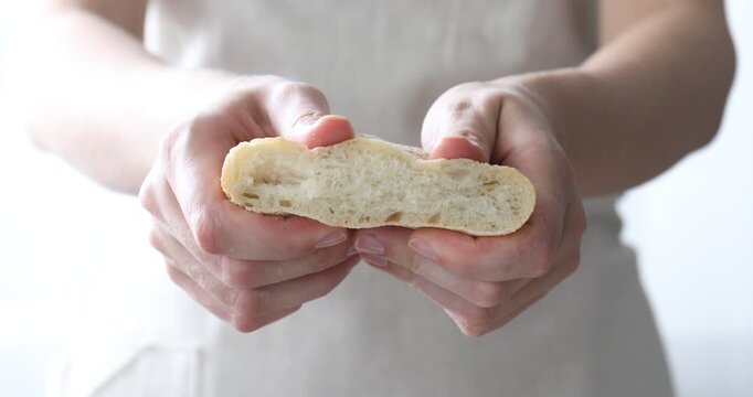 Woman squishing piece of fresh ciabatta on light background, closeup