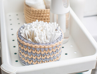 Woven basket filled with cotton swabs sits on a bathroom tray alongside a spray bottle and additional storage, showcasing organized personal care essentials