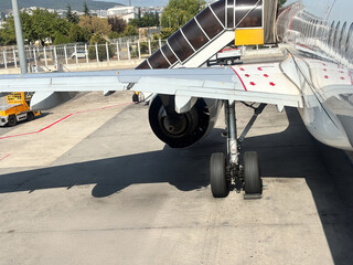 Aircraft wing with engine and landing gear visible on tarmac, showcasing aviation technology and maintenance, with ground service equipment in the background