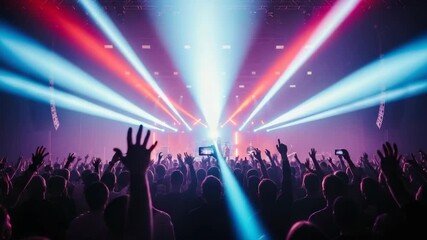 live concert A large crowd raises hands some recording with phones Dynamic stage lights with powerful beams of red blue and white illuminate the hazy venue highlighting performers on stage
