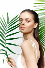 Fototapeta premium Beautiful woman with long hair and natural makeup holding a palm leaf, exuding confidence and warmth in a tropical setting.