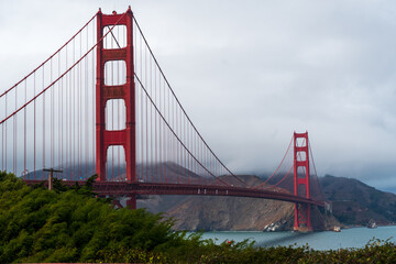 The Golden Gate Bridge in San Francisco, California, with its iconic red towers rising above the bay on a cloudy day.