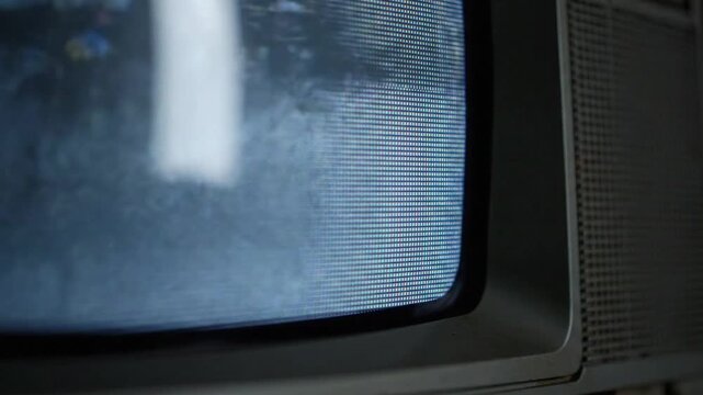 Close-up of an old CRT television screen with static noise and distortion. Retro vintage analog TV screen turning on with signal interference and a snowy display.