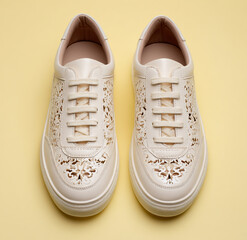 Pair of elegant cream leather perforated sneakers on a yellow background