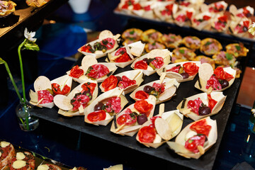 Mini Charcuterie Canapés with Cured Meats, Cheese, Olives and Tomato in Wooden Boats on Slate Tray