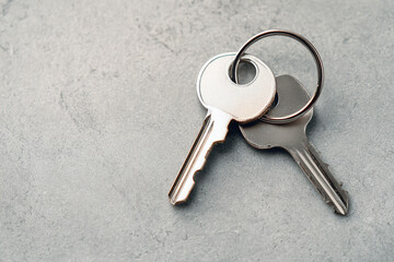 Two silver keys on a metal ring on a textured gray surface