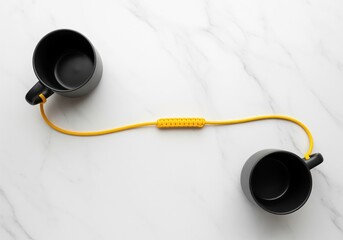 Two matte black ceramic mugs connected by a vibrant yellow braided cord on a white marble surface