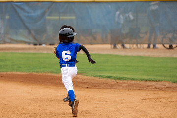 A young boy, age six or seven, ran toward first base. Baseball field. Boy playing baseball.