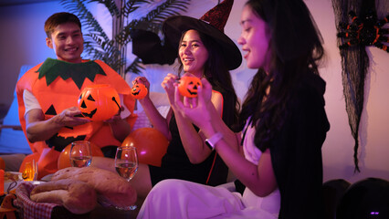 Friends at a Halloween party hold mini pumpkin buckets and smile during a festive moment.