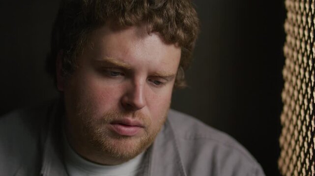 Young remorseful man talking calmly through ornate lattice screen during confession in church. Close-up shot