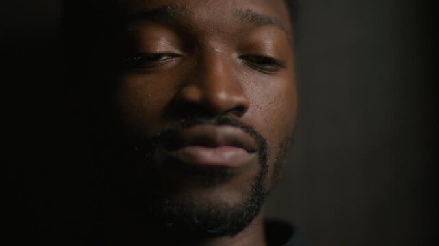 Young Black male priest reading aloud from Bible while offering spiritual guidance to parishioner during confession. Close-up shot