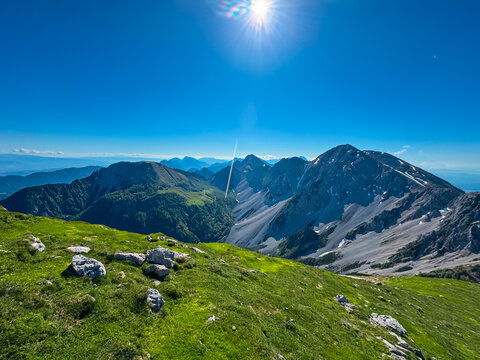 From a grassy vantage point on Weinasch, a spectacular panoramic view unfolds across the rugged peaks and deep valleys of the Karawanks mountain range on a perfect, sun-drenched summer day. - Powered by Adobe