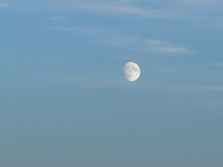 Daytime moon visible high above the quiet prairie horizon on a clear afternoon.
