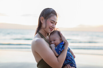 Asian Young woman holding baby mother and child beach background loving embrace sunset lighting happy family moment affectionate care ocean shore maternal bond smiling woman