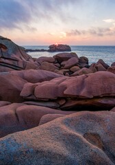 Stunning sunset over the Pink Granite Coast in Brittany, France. Unique weathered rock formations and ocean waves create a magical seascape in soft evening light.