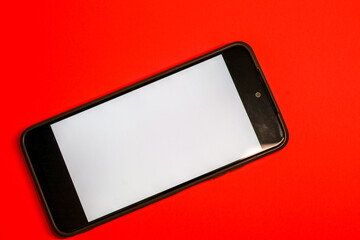 ​A smartphone with a clean white screen is positioned diagonally on a vivid red background,...