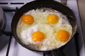 Four egg yolks of perfectly round shape are frying in an old cast-iron pan on a white stove, creating a hearty breakfast. This close-up shot captures the process of cooking, highlighting the vivid col