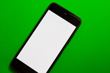 A smartphone with a clean white screen is positioned diagonally on a vivid green background,...