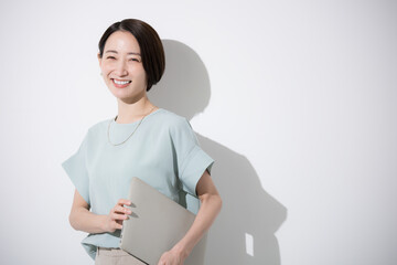 Obraz premium パソコン持つオフィスカジュアルで立つカメラ目線の美人な女性のビジネスイメージ上半身、白背景 笑顔、微笑む