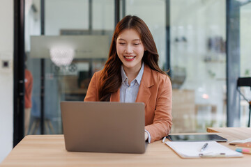 Fototapeta premium Asian Businesswoman Using laptop computer and working at office with calculator document on desk, doing planning analyzing the financial report, business plan investment, finance analysis concept.