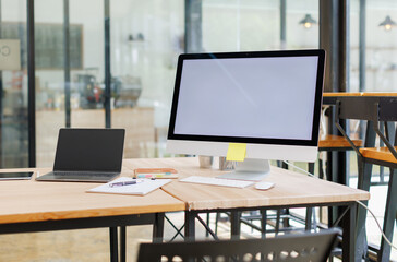 Open desktop with blank screen view of a white-screen desktop computer mockup and accessories on a wooden desk in a workplace office room. private office, office workspace.

