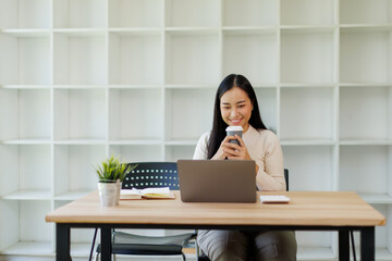 Stylish young asian female freelancer working on laptop while sitting in cozy cafe
