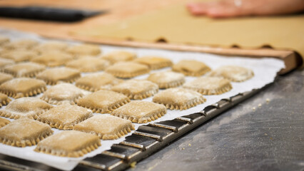 Close up of freshly made ravioli squares dusted with flour arranged on a baking sheet in a rustic...