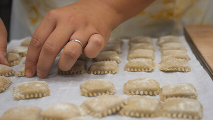 Close up on hands meticulously arranging fresh pasta ravioli on a white tray in a small business kitchen preparing traditional Italian cuisine with passion