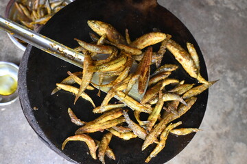 Small Snakehead or Channa orientalis Fish being fried in a pan. Fish are typically marinated with spices like turmeric, salt, and chili powder before being deep fried until they are crispy and golden.