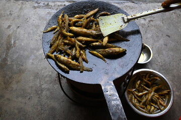 Small Snakehead or Channa orientalis Fish being fried in a pan. Fish are typically marinated with spices like turmeric, salt, and chili powder before being deep fried until they are crispy and golden.