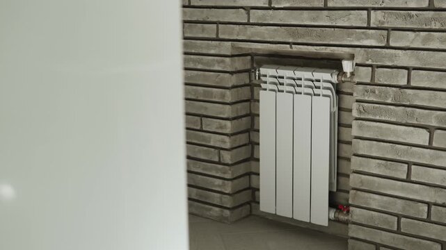 Modern bimetallic heating radiator in brick effect wall with condensation falling from cold air. Central heating system with temperature controller for savings on bills.