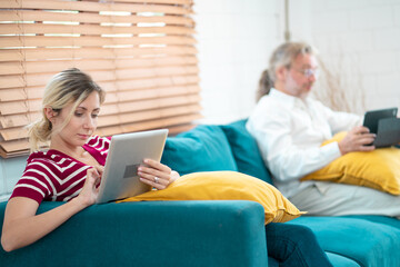 Young woman and grandfather using digital tablet at home. Freelancer holding and using digital tablet, sitting at cozy sofa in living room. Online technology. Remote job
