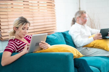 Young woman and grandfather using digital tablet at home. Freelancer holding and using digital tablet, sitting at cozy sofa in living room. Online technology. Remote job