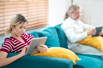 Young woman and grandfather using digital tablet at home. Freelancer holding and using digital tablet, sitting at cozy sofa in living room. Online technology. Remote job