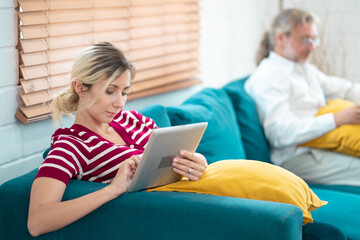 Young woman and grandfather using digital tablet at home. Freelancer holding and using digital tablet, sitting at cozy sofa in living room. Online technology. Remote job