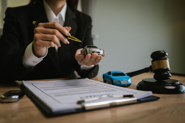 Close-up of a lawyer working on a contract with a gavel placed on a toy car, symbolizing automobile law and justice.
