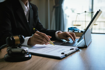 Close-up of a lawyer working on a contract with a gavel placed on a toy car, symbolizing automobile law and justice.