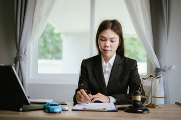 Female lawyer reviewing legal documents at office desk with gavel, justice scale, and contract...