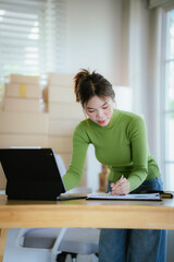 A young female entrepreneur managing online orders, packing parcels, and running a small e-commerce business with professionalism and happiness.