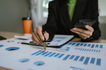 Businesswoman analyzing financial charts with calculator and documents on desk, working on business data and financial report in modern office.