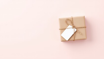 Minimalist composition featuring a neatly wrapped gift box with a blank label and string on a soft pink background