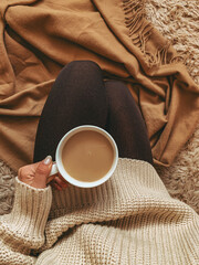 A woman in a sweater holds a cup of coffee