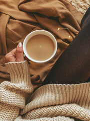 A woman in a sweater holds a cup of coffee
