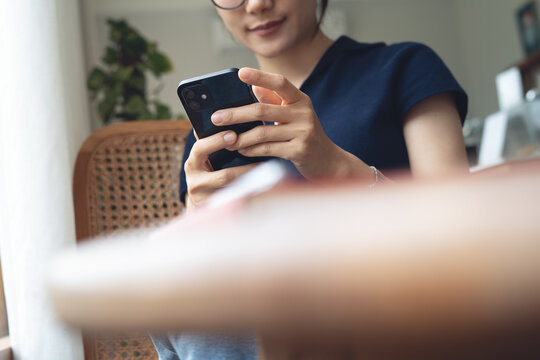 Young asian woman sitting at table using smartphone in coffee shop. Woman using mobile phone for online shopping and internet payment via mobile app or social networking